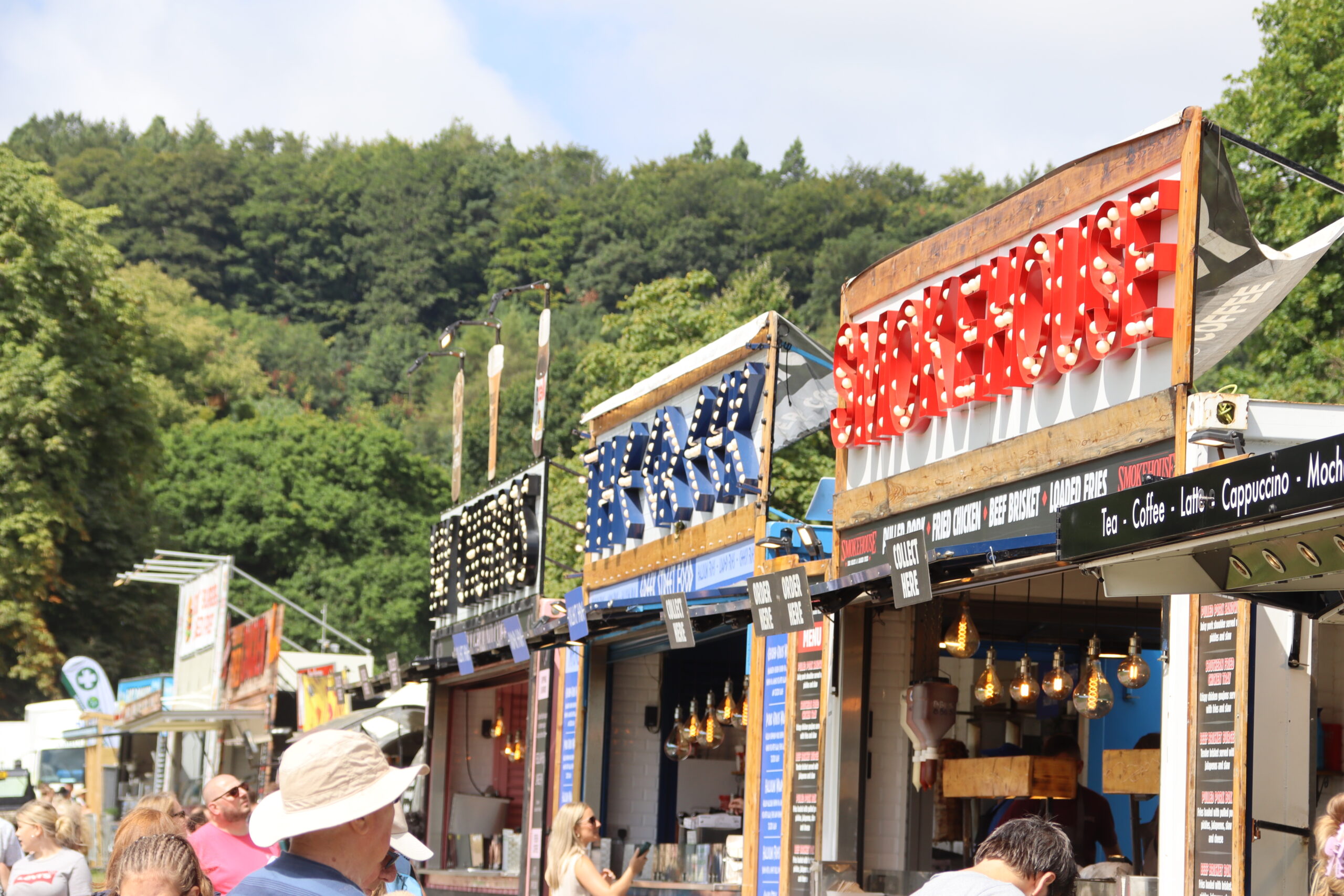 Row of food tents set up at a festival, with people walking and gathering in front of the stalls.