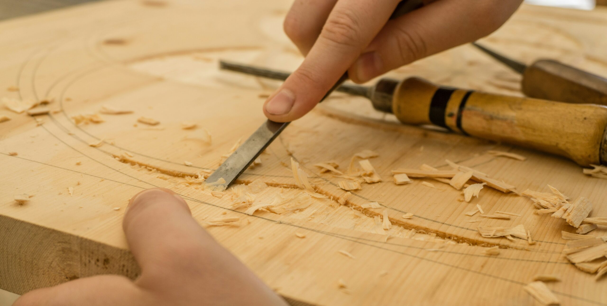 Close-up of wood carving in progress. A hand is using a chisel to carve intricate designs into a wooden surface.