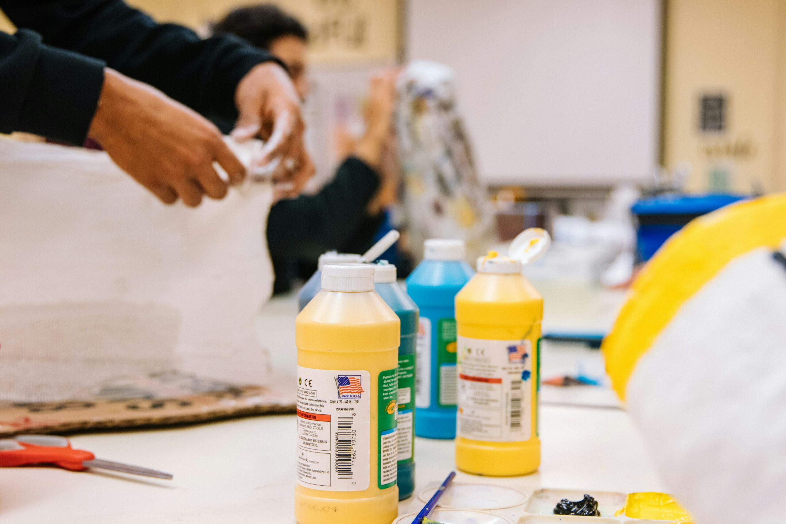 A workspace filled with vibrant bottles of paint, brushes, and scissors, highlighting the preparation for a craft activity or art project.