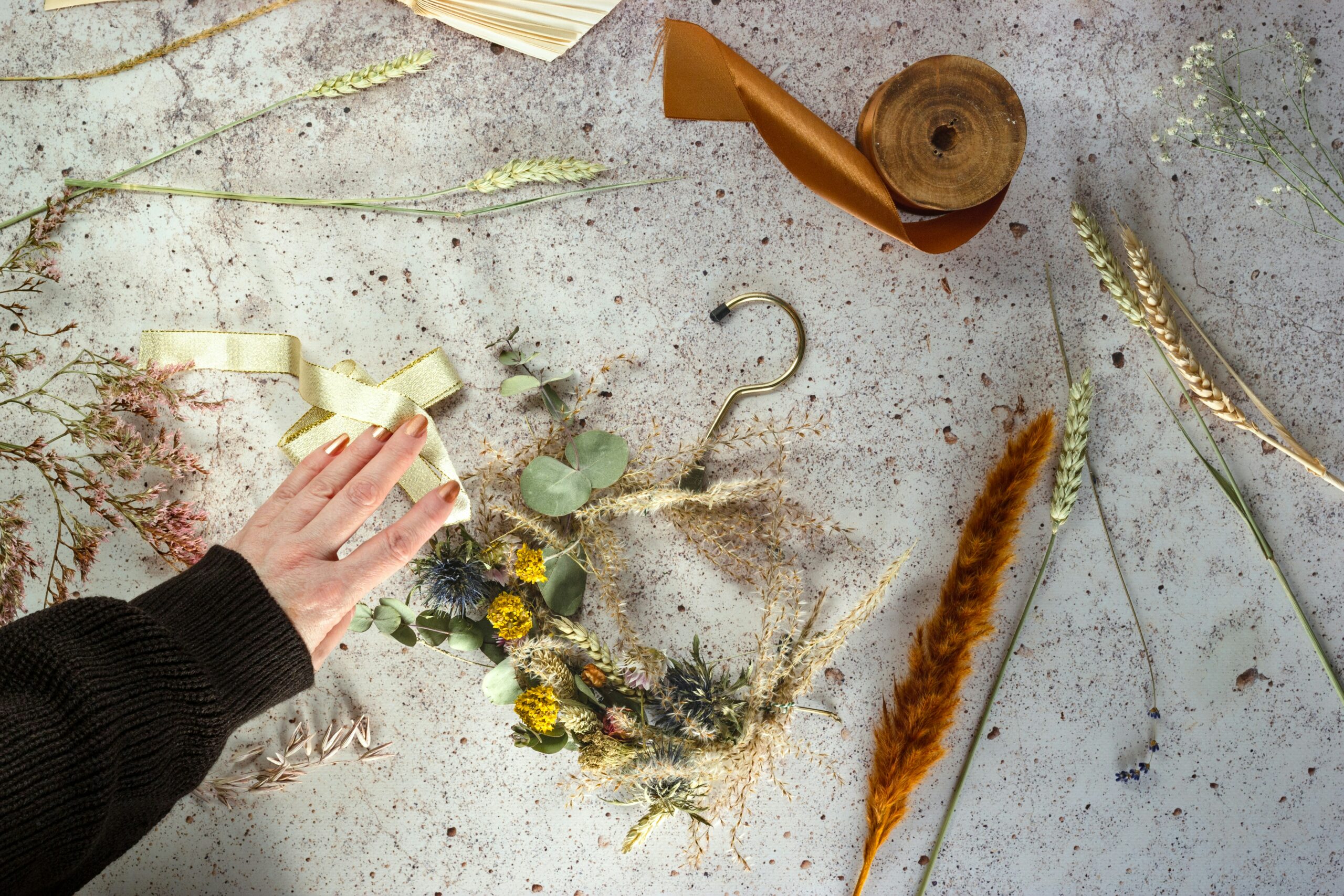 A flat-lay of dried flowers, ribbons, and a metal hanger, illustrating materials for a craft project to create a decorative wreath.