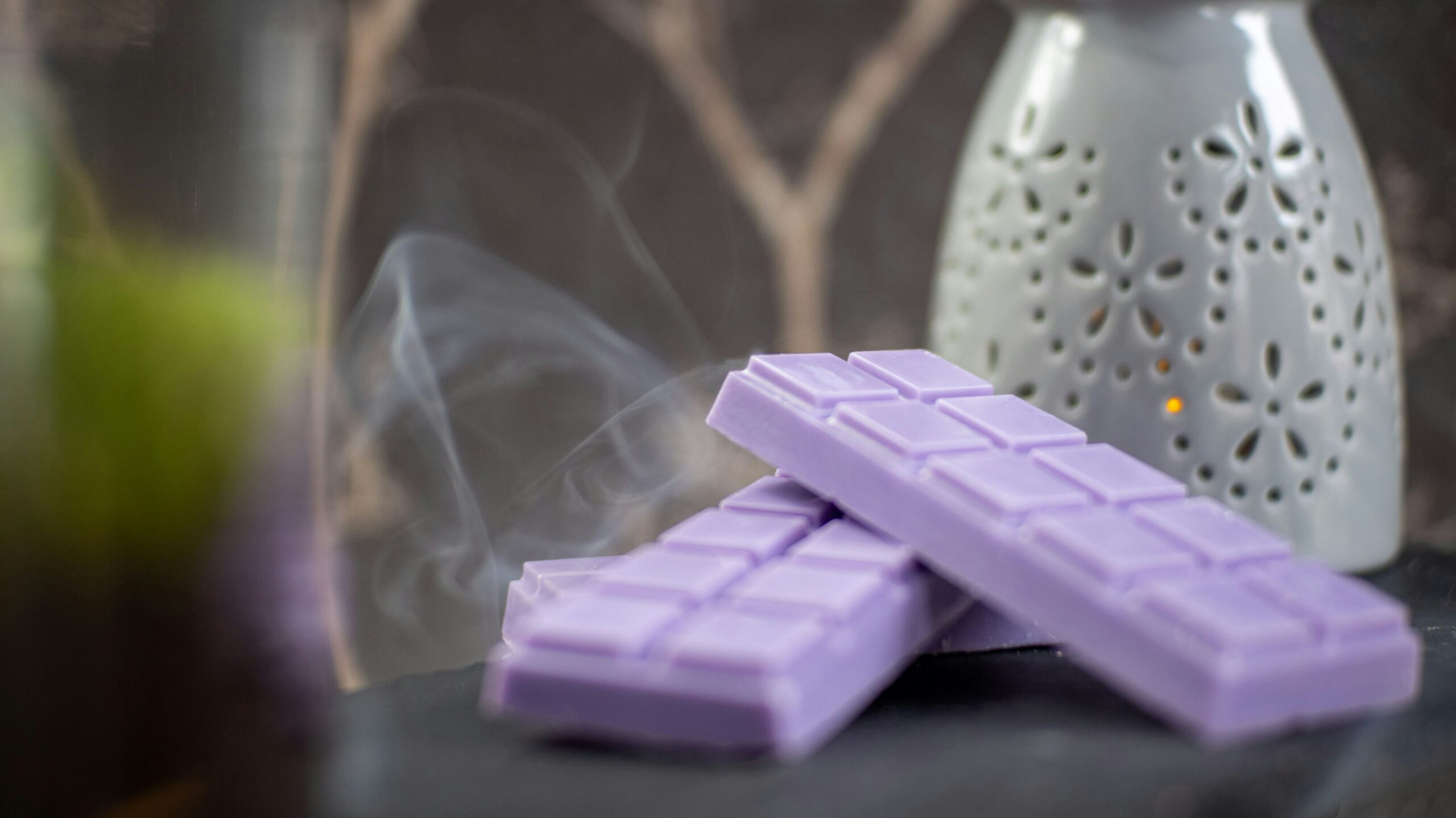 Two purple wax melt bars releasing scented smoke, with a decorative white wax warmer in the background.